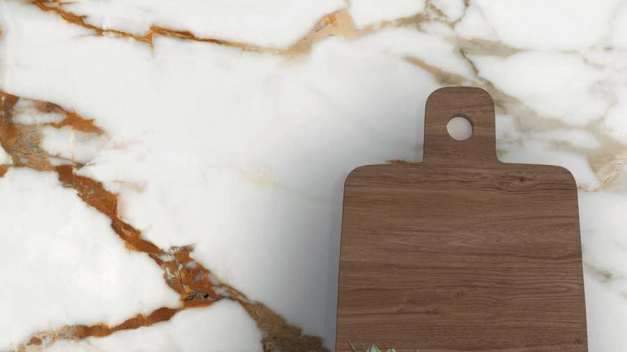 Plancha de porcelánico blanco con vetas doradas y grises, con una tabla de madera apoyada encima