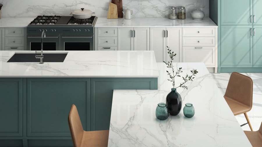 Cocina con muebles verdes, isla y mesa de porcelánico blanco con vetas grises