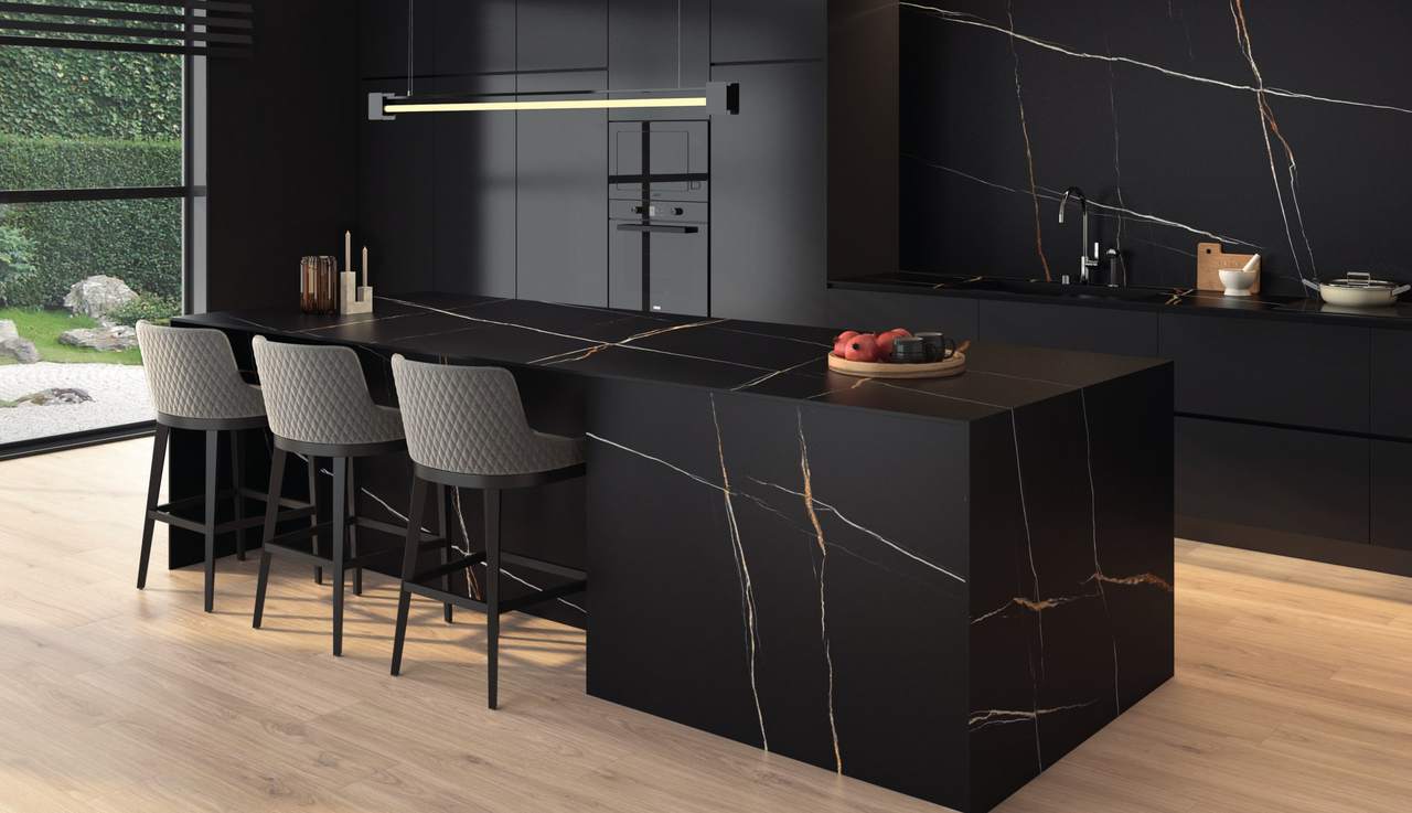 Cocina negra con isla de porcelánico negro con vetas blancas y doradas que siguen por el lateral