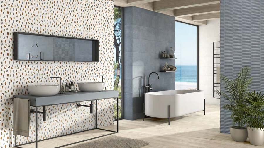 Baño con una pared de azulejo blanco decorado con trazos de colores, una pared lisa gris y otra blanca con relieve, sobre suelo de lamas de madera