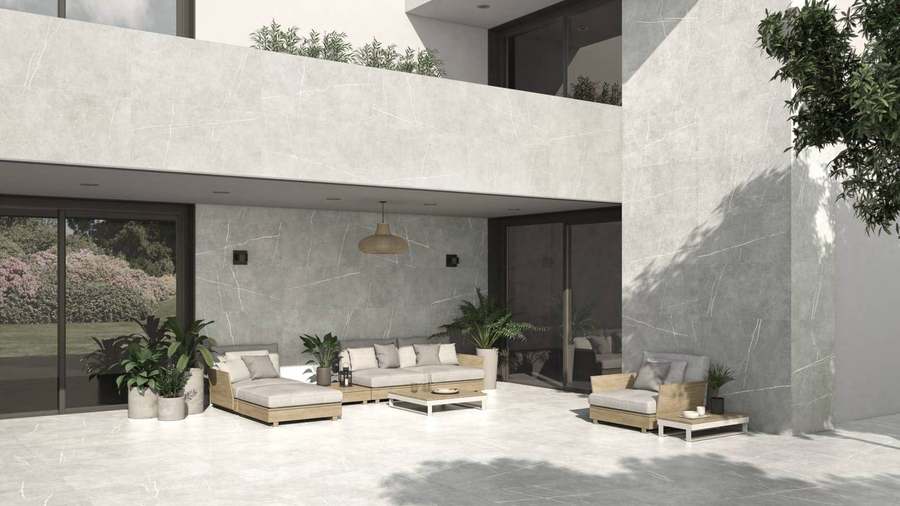 Terraza cubierta con paredes y suelo de porcelánico gris de aspecto piedra, con sofás y plantas