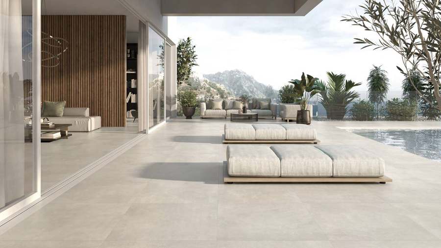 Salón abierto a una terraza con piscina, con el mismo suelo gris claro de aspecto cemento dentro y fuera